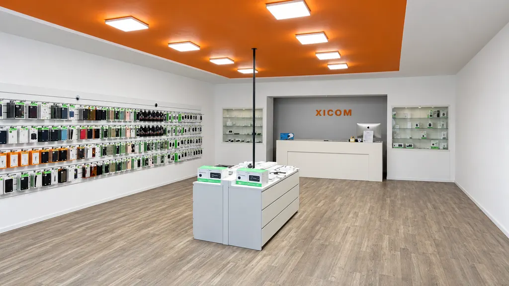 De winkel van Xicom van binnen: een wand vol hoesjes en accessoires, een oranje plafond en de balie met het Xicom-logo