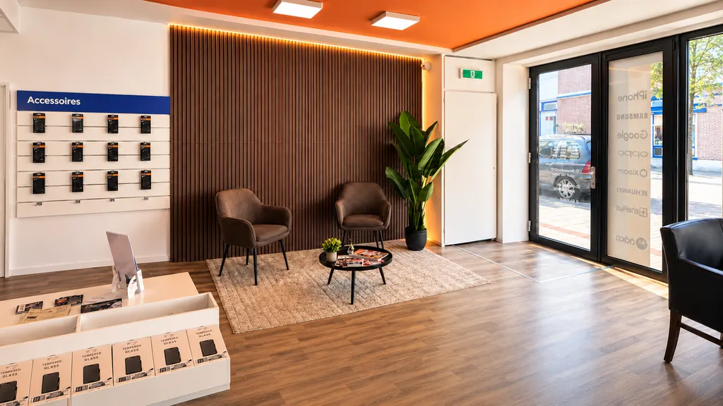De wachthoek in de winkel van Xicom: twee leren stoelen, een plant en een salontafel voor een houten wand met warme verlichting